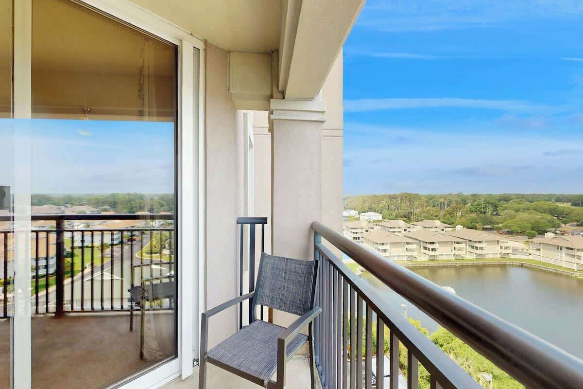A balcony with a chair, a glass door, and a view of a river and buildings.