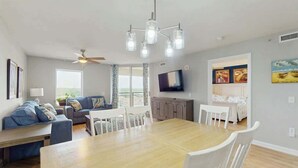 Una sala de estar moderna con comedor, ventilador de techo, televisor de pantalla plana y obras de arte en las paredes.