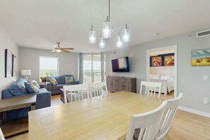 A modern living room with a dining area, a ceiling fan, a flat-screen TV, and artwork on the walls. - Tilghman Condos #1018 (North Myrtle Beach)