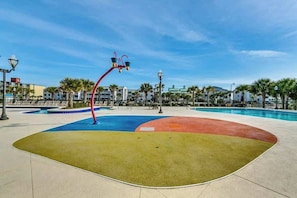 A swimming pool area with a colorful design, surrounded by palm trees and lounge chairs. - Tilghman Condos #1217 (North Myrtle Beach)