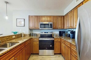 A kitchen with wooden cabinets, a stainless steel microwave, an oven, and a refrigerator. - Tilghman Condos #1217 (North Myrtle Beach)
