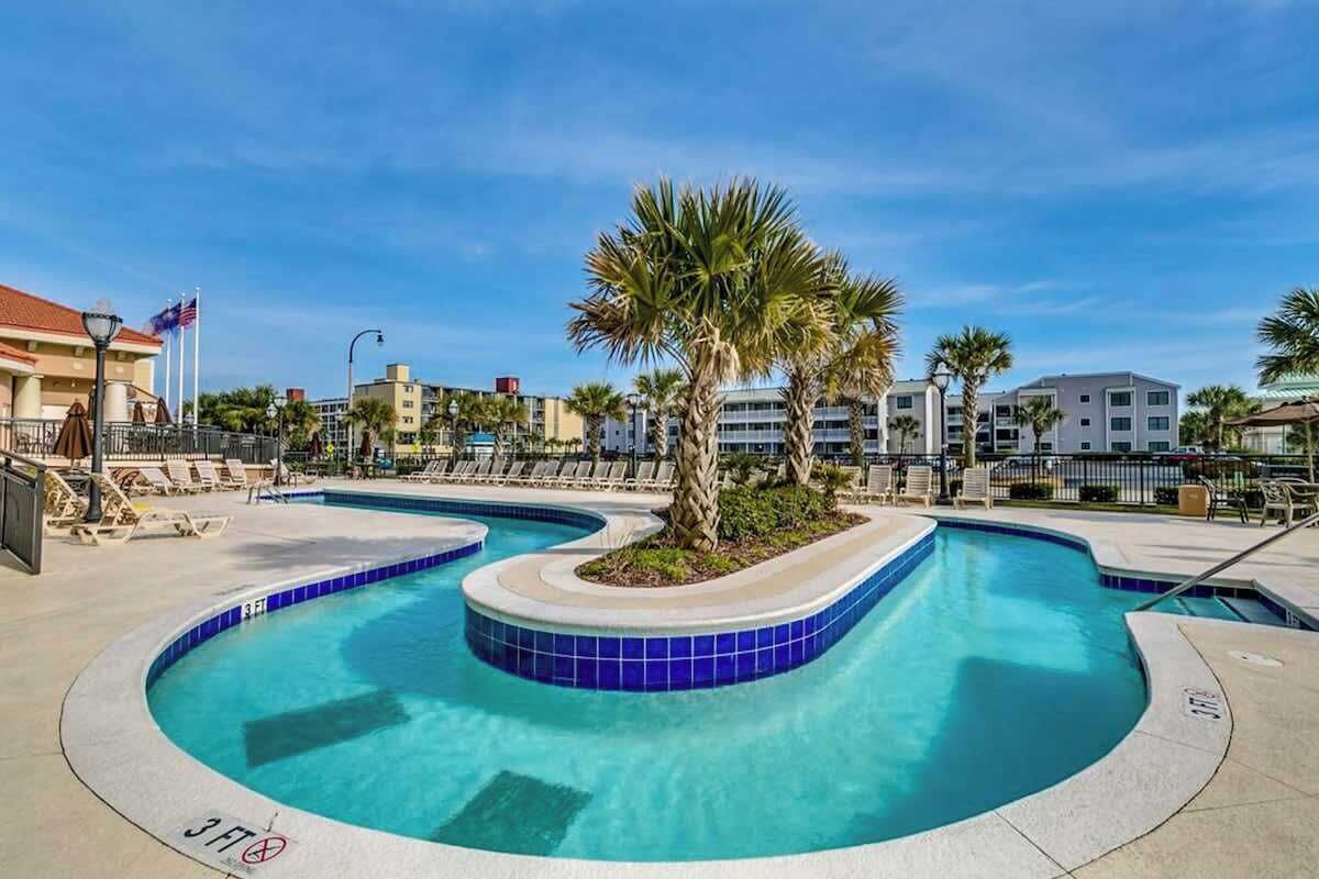 A swimming pool with a curved design, surrounded by lounge chairs and palm trees.