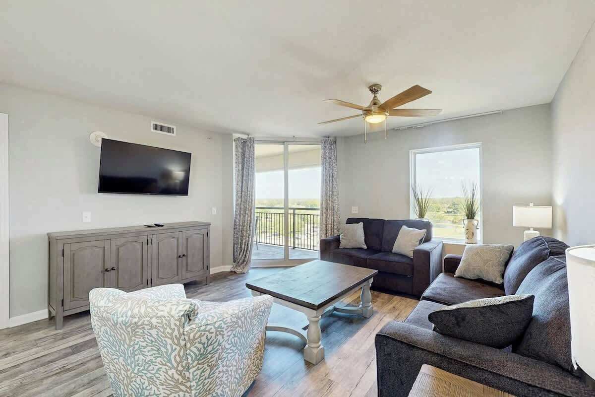 A living room with a flat-screen TV, a ceiling fan, a sofa, a coffee table, and a window with a view.
