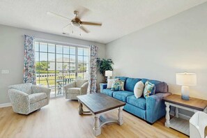 A living room with a blue sofa, patterned armchairs, a wooden coffee table, and a ceiling fan. - Palmy Days at Ironwood 424 (North Myrtle Beach)