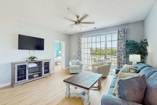 A living room with a flat-screen TV, a wooden coffee table, a sofa, and a ceiling fan. - Palmy Days at Ironwood 424 (North Myrtle Beach)