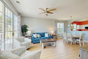 A spacious living room with a blue sofa, a coffee table, and a dining area with a table and chairs. - Palmy Days at Ironwood 424 (North Myrtle Beach)