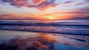 Ein Sonnenuntergang über einem Strand, wobei Wellen den Himmel widerspiegeln.
