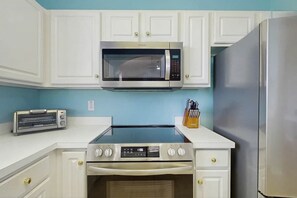A kitchen with white cabinetry, a microwave, a toaster, a stove, and a refrigerator. - Starfish Retreat at The Havens 1434 (North Myrtle Beach)
