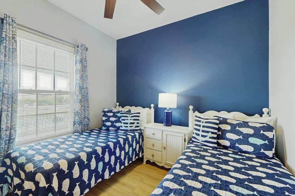 Un dormitorio con dos camas, una mesita de noche y un ventanal con cortinas.