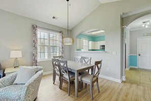 A dining area with a wooden table and chairs, a hanging light fixture, and a window with curtains. - Starfish Retreat at The Havens 1434 (North Myrtle Beach)