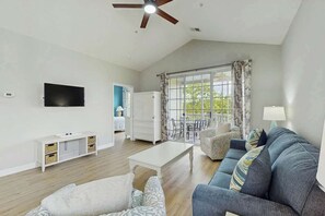 A spacious living room with a ceiling fan, a flat-screen TV mounted on the wall, a sofa, a coffee table, and a dining area with a table and chairs. - Starfish Retreat at The Havens 1434 (North Myrtle Beach)