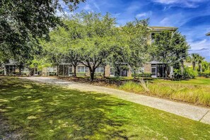 A building with a paved pathway leading to the entrance, surrounded by trees and grass. - Starfish Retreat at The Havens 1434 (North Myrtle Beach)