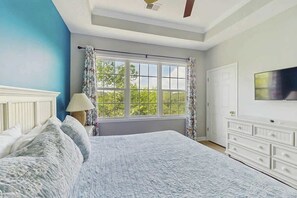 A bedroom with a large bed, a window with curtains, a television on the wall, and a white dresser. - Starfish Retreat at The Havens 1434 (North Myrtle Beach)