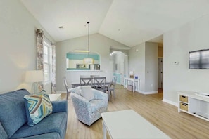 A modern living room with a sofa, armchair, and a dining area with a table and chairs. - Starfish Retreat at The Havens 1434 (North Myrtle Beach)
