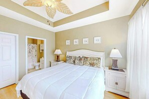 A bedroom with a bed, two bedside tables, a ceiling fan, a door, and a bathroom visible through an open door. - Chillville Unit 1635 (North Myrtle Beach)