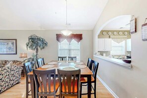 Uma área de jantar com mesa e cadeiras de madeira, luminária pendente e janela com persianas.