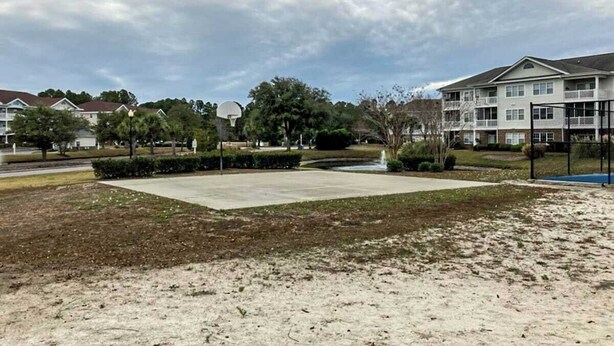 Un quartier résidentiel avec un terrain de basket, une fontaine et des immeubles d’habitation en arrière-plan.
