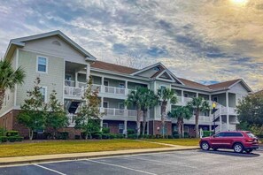 A multi-story residential building with balconies, a parking lot, and a red vehicle parked in front. - Chillville Unit 1635 (North Myrtle Beach)