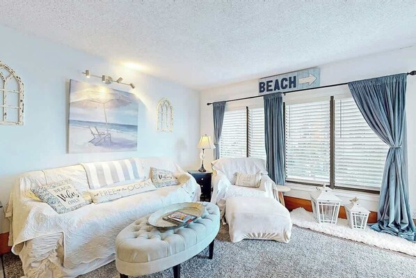 Un salon décoré sur le thème de la plage, avec un canapé, un fauteuil, un pouf et un panneau indiquant le mot « PLAGE ».