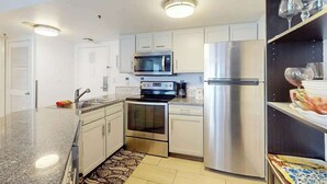 A modern kitchen with stainless steel appliances, white cabinetry, and a patterned rug. - Cozy Beach Rendezvous at The Palace Resort (Myrtle Beach)