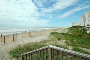 Ein Strand mit einer Holzpromenade, die zu einem mehrstöckigen Gebäude führt.