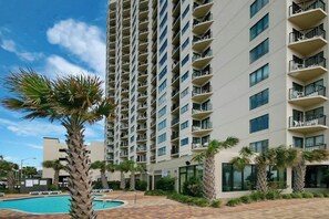 Un hôtel de grande hauteur doté de nombreux balcons, d’une piscine et de palmiers.