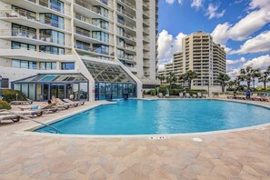 A swimming pool with lounge chairs and a glass-enclosed area, surrounded by a multi-story building with balconies. - Ocean Creek Plantation EE6 (Myrtle Beach)