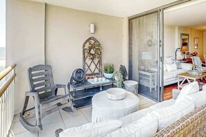 Un balcon avec un coin salon, une table équipée d’un ventilateur et un élément décoratif mural.