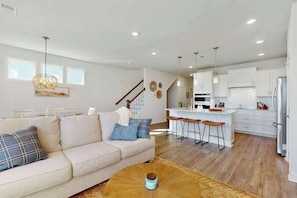 A modern living room with a sofa, coffee table, and a kitchen area with bar stools and a refrigerator. - Double Eagle Unit 15 (North Myrtle Beach)