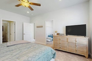 Ein Schlafzimmer mit einem Bett, einem Schminktisch, einem Fernseher und einem Deckenventilator.