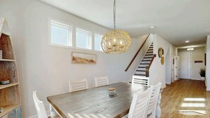Et spiseområde med et træbord og hvide stole, en hængende lampe og en trappe til et andet rum.