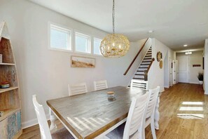 Ein Essbereich mit einem Holztisch, weißen Stühlen, einer Hängelampe und einer Treppe, die in einen anderen Raum führt.