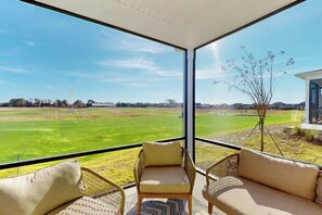 Ein Balkon mit Korbmöbeln und Blick auf ein grünes Feld.