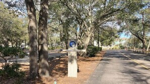 A signpost with the text 'Lodge East' and a logo, surrounded by trees and a road. - Ocean Creek Unit 2359 (Myrtle Beach)