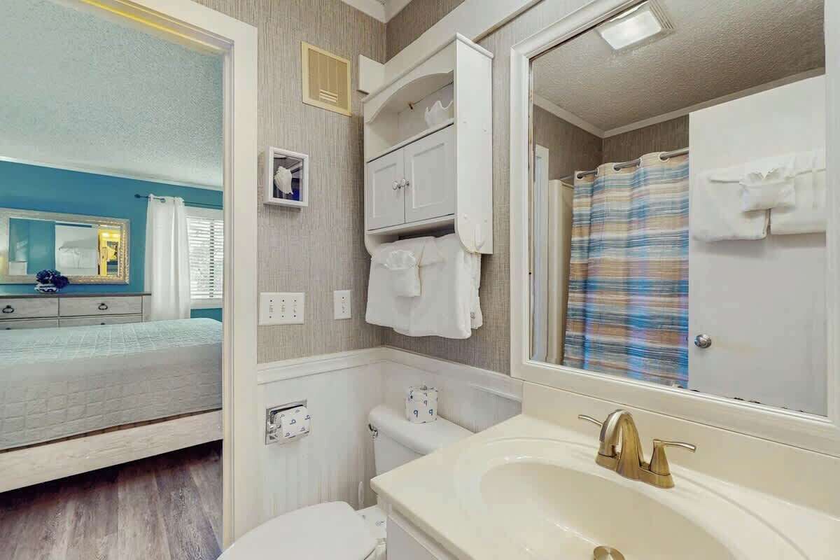 A bathroom with a sink, mirror, toilet, and shower curtain.