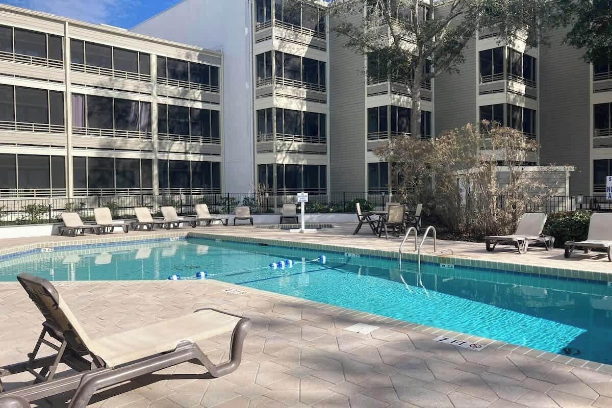 A swimming pool with lounge chairs and a building with multiple floors and windows.