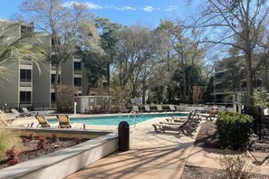 Zona de piscina con sillones reclinables y un edificio al fondo.