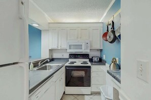 Een kleine keuken met witte kastjes, een magnetron, fornuis en waterkoker.
