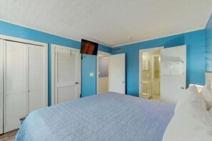 Un dormitorio con cama, televisor montado en la pared y puerta de baño.