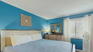 A bedroom with a bed, a dresser, a mirror, a wall decoration, and a window with curtains. - Ocean Creek Unit 2359 (Myrtle Beach)