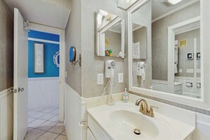 Un baño con un lavamanos blanco, un espejo grande y un secador de pelo en la pared.