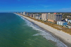 Eine Küstenstadt mit einem langen Strand, Hochhäusern und blauem Himmel.