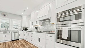 A modern kitchen with white cabinetry, stainless steel appliances, and a herringbone-patterned wood floor. - Hermosa Villa Retreat (North Myrtle Beach)