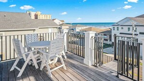 A wooden deck with a table and chairs, overlooking a beach and buildings. - Hermosa Villa Retreat (North Myrtle Beach)
