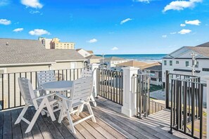 Eine Holzterrasse mit Tisch und Stühlen mit Blick auf einen Strand und Gebäude.