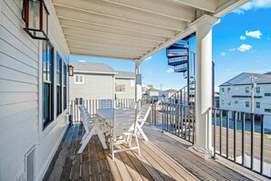 A covered balcony with a wooden deck, white outdoor furniture, and a view of neighboring buildings. - Hermosa Villa Retreat (North Myrtle Beach)