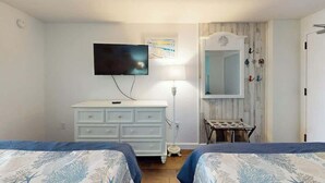 Et soveværelse med to senge, en kommode, et fjernsyn, en lampe og et spejl.