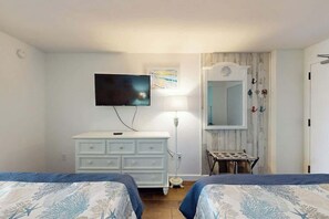 Ein Schlafzimmer mit zwei Betten, einem Schminktisch, einem Fernseher, einer Lampe und einem Spiegel.