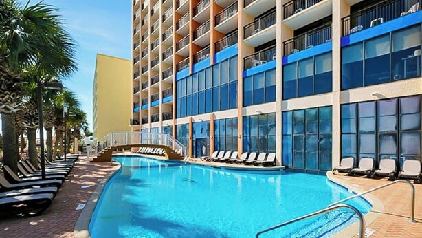 Et hotel med swimmingpool, liggestole og en bygning med flere etager og altaner.