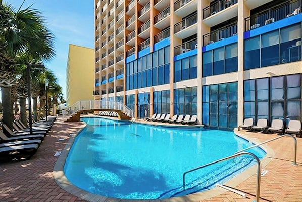 Ein Hotel mit Swimmingpool, Liegestühlen und einem mehrstöckigen Gebäude mit Balkonen.